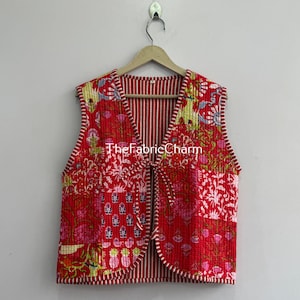 Può includere: Un gilet trapuntato senza maniche con un vivace motivo patchwork rosso con disegni floreali e di ananas. Il capo presenta uno scollo a V, chiusure con lacci frontali e bordi a righe rosse e bianche. Il testo TheFabricCharm è visibile sul davanti.