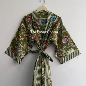 以下が含まれることがあります： ピンク、ブルー、イエローの色合いの鮮やかな花柄が特徴のオリーブグリーンのローブ。結び紐付きのベルト、ストライプ柄の袖口を備えた幅広の袖、ストライプ柄の襟が特徴です。前面にはTheFabricCharmという文字がプリントされています。