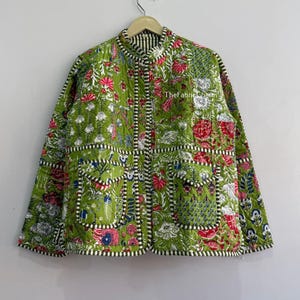 May include: A quilted jacket featuring a vibrant green base with a multi-colored floral and botanical print in shades of pink, white, and blue. The garment includes a mandarin collar, long sleeves, two front pockets, and black and white striped trim.