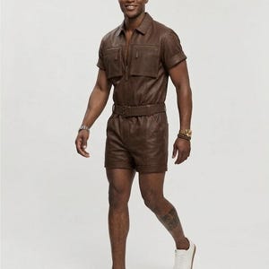 May include: A brown leather romper with short sleeves, a collared neckline, and a belted waist. The romper features a zipper closure and two chest pockets. The person is wearing white sneakers.