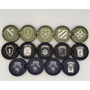 May include: A collection of round, military-themed items, each featuring a different emblem or insignia. The items are in shades of green, black, and navy blue, with white and silver details. The designs include a lightning bolt, a mountain scene, and the word "Airborne".