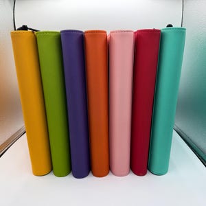May include: A row of colorful, vertical zippered pouches in shades of yellow, green, purple, orange, pink, red, and teal. The pouches are made of a smooth material and are arranged in a line against a white surface.