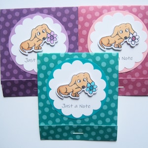 May include: Three greeting cards with a polka dot background. Each card features a cartoon dachshund holding a flower. The text on the cards reads "Just a Note".