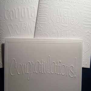 May include: White card with embossed lettering that reads "Congratulations!" The card is blank inside and is perfect for writing a message.
