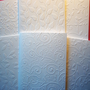 May include: A stack of six white embossed cards with different floral patterns. The cards are all the same size and are arranged in a vertical stack.