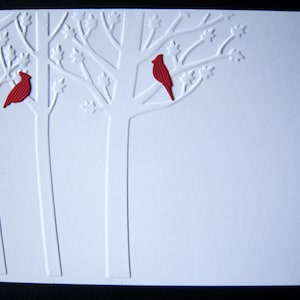 May include: A white card with a raised embossed design of trees and red cardinals. The card is blank and ready for a message.