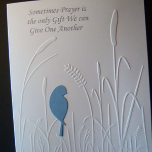 May include: A white card with a blue bird silhouette and embossed white grass and reeds. The card reads "Sometimes Prayer is the only Gift We can Give One Another."