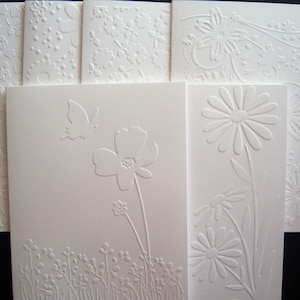 May include: Set of six white embossed cards with floral and butterfly designs. The cards are blank and perfect for writing messages.
