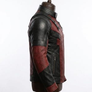 May include: A two-tone leather jacket in black and burgundy, displayed on a mannequin. The jacket features a stand-up collar, shoulder accents, and a zippered pocket. The sleeves are black, and the body is burgundy.