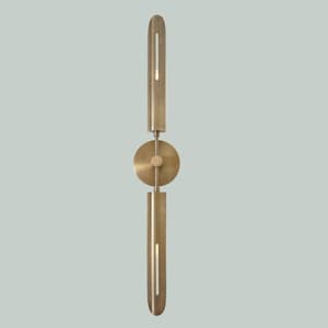 May include: A modern, brass-toned wall sconce with a minimalist design. The sconce features two elongated, cylindrical elements, one above and one below a circular disc. Each cylinder has a vertical slit, likely for light emission.