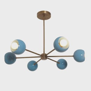 Könnte beinhalten: Eine moderne Deckenleuchte mit Messing-Finish und sechs hellblauen Kugelschirmen. Die Leuchten sind in einem Sternmuster angeordnet, wobei jede Kugel eine helle Glühbirne enthält. Die Leuchte ist für die Deckenmontage konzipiert.