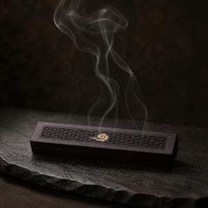 Peut inclure: Une boîte brûle-encens rectangulaire en bois brun foncé avec un motif en treillis décoratif sur le couvercle et un petit emblème de nuage doré au centre, d'où s'élèvent de fines volutes de fumée blanche depuis la surface supérieure.