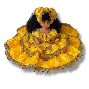 May include: A doll in a vibrant yellow dress with a ruffled skirt and a matching headscarf. The dress is trimmed with gold and colourful beads. The doll has black curly hair and blue eyes.