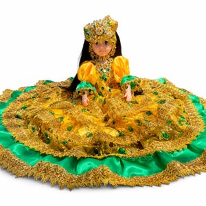 May include: A doll with long dark hair wearing a yellow and green dress with gold lace trim and sequins. The doll features a matching ornate headpiece and a bodice decorated with green and gold embellishments, with a wide, layered skirt.