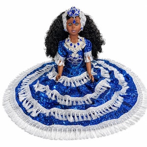May include: A doll with dark curly hair wearing a vibrant blue sequined dress featuring multiple tiers of silver fringe trim. The doll is adorned with a matching silver and blue jeweled headpiece and a coordinating necklace, creating a cohesive look.