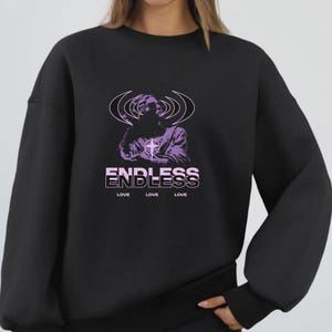 May include: Black sweatshirt featuring a purple graphic of a figure with radiating lines and a cross. The word "ENDLESS" is stacked above three instances of the word "LOVE" in a white sans-serif font. A casual, comfortable style.