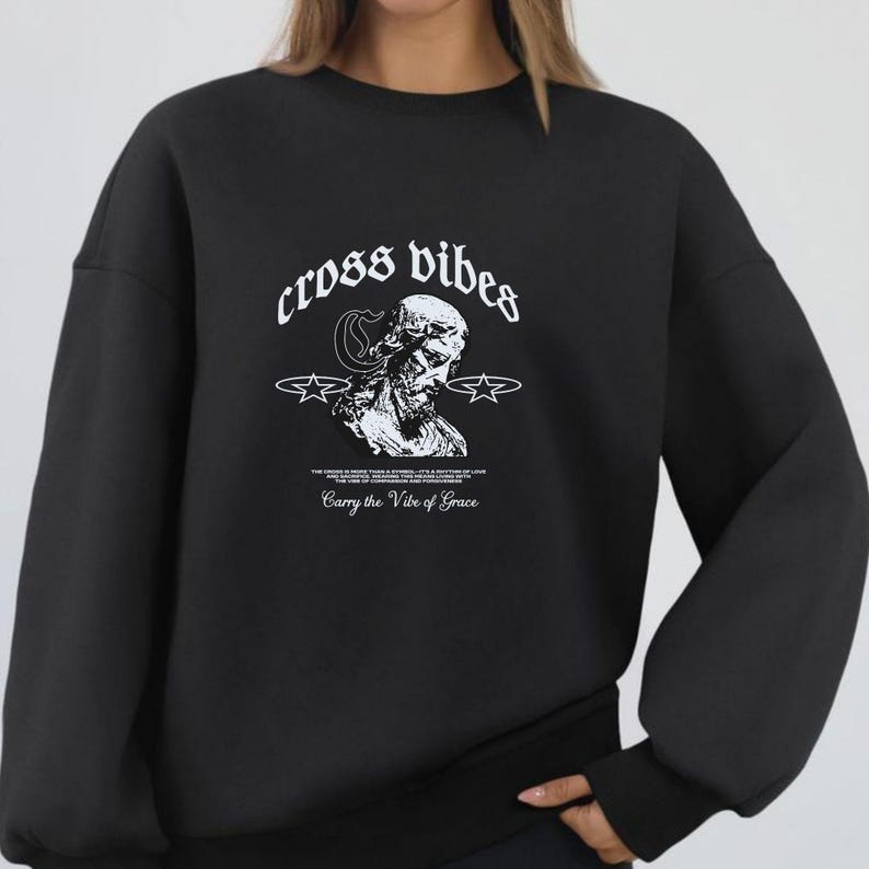May include: Black sweatshirt with the text "cross vibes" in a stylized font above a black and white graphic of a religious figure. The phrase "Carry the Vibe of Grace" is printed below the graphic.