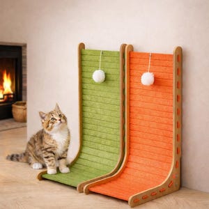 Könnte beinhalten: Ein neugieriges getigertes Kätzchen sitzt neben zwei Kratzbäumen. Einer ist grün, der andere orange, beide mit Holzrahmen und einem hängenden weißen Pompon-Spielzeug. Die Katze schaut nach oben, als würde sie das Spielzeug betrachten.