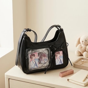 Peut inclure: Un sac à bandoulière noir doté de deux poches avant transparentes pour exposer des objets de collection. Le sac comprend un nœud décoratif noir sur le côté droit et une bandoulière réglable. Les poches transparentes contiennent des cartes.