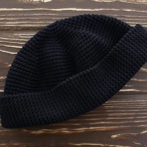 May include: A navy blue knit beanie hat with a folded brim. The hat is made of a textured knit fabric and is displayed on a wooden surface. This winter hat is a stylish accessory.
