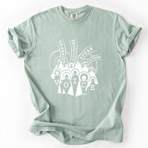 May include: A light green t-shirt with a white graphic design. The design features the word "VOICE" with figures and the words "MINDFUL ATTITUDES SPEAK KINDNESS". The shirt is made of a soft material and has a crew neck.