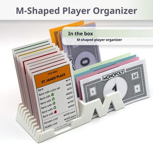 May include: A white M-shaped player organizer holding various Monopoly game cards and paper money. The organizer features a series of slots for card storage. Text on the image includes M-Shaped Player Organizer, In the box, and M-shaped player organizer 1 pc.