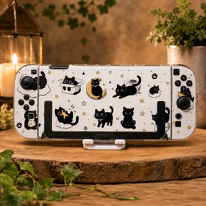 May include: A white gaming console skin featuring a pattern of black cats in various poses, including sitting in a box, resting on a crescent moon, and playing with stars. The design includes small yellow star accents and paw prints on a light background.