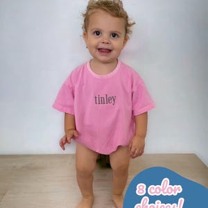 May include: A pink toddler t-shirt with the name "tinley" embroidered on the front. The t-shirt is available in 8 colors.