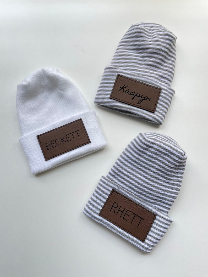 May include: Three white and grey striped knit hats with brown leather patches. The patches have the names "Kaspyan", "Beckett", and "Rhett" written on them.