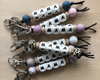 May include: Four keychains with wooden beads and colorful silicone beads. Each keychain has the word "MAMA" spelled out on white beads. The keychains are attached to silver key rings.