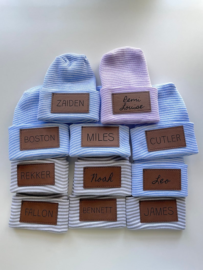 May include: Ten striped baby hats with personalised leather name tags. The hats are in shades of blue and grey. The names on the tags are Zaiden, Remi Louise, Boston, Miles, Cutler, Rekker, Noah, Leo, Fallon, Bennett, and James.