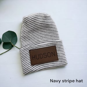 May include: A white and navy striped beanie with a brown leather patch that says "HUDSON" on it. Navy stripe hat.