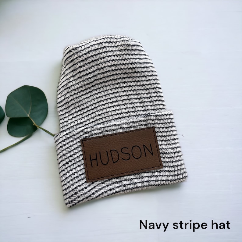 May include: A white and navy striped beanie with a brown leather patch that says "HUDSON" on it. Navy stripe hat.