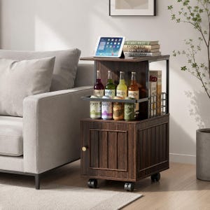 May include: A dark wood rolling side table with a cabinet base, an open middle shelf holding eight glass bottles, and a top surface featuring a tablet and a stack of books. The unit has a black metal frame, a small gold knob, and four caster wheels.