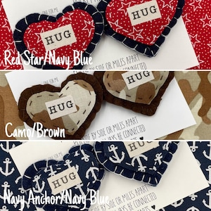 Pu&ograve; includere: Due ornamenti a forma di cuore in feltro con la scritta "HUG" su di essi. I cuori sono decorati con stelle rosse e tessuto blu navy. Il testo "Red Star/Navy Blue" &egrave; anche visibile nell'immagine.