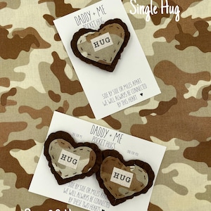Pu&ograve; includere: Set di due abbracci tascabili a forma di cuore in tessuto mimetico marrone e beige con la parola "HUG" cucita su ciascuno. I cuori sono su una carta bianca con il testo "Daddy + Me Pocket Hugs" e "Lato a lato o a chilometri di distanza, saremo sempre connessi da questi due cuori".
