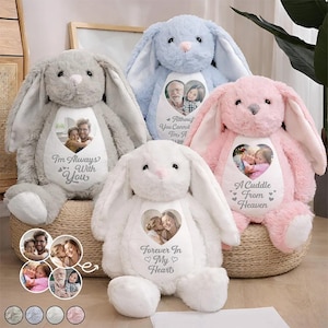 May include: Four plush bunny toys in grey, blue, white, and pink, each featuring a white heart-shaped patch on the chest. The patches display printed photographs of people and text including "I'm Always With You," "You Cannot," "A Cuddle From Heaven," and "Forever In My Heart."