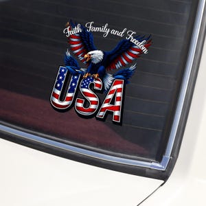 May include: A patriotic decal featuring a bald eagle with outstretched wings, colored in red, white, and blue. The word "USA" is prominently displayed below the eagle, with the text "Faith Family and Freedom" above.