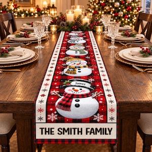 May include: A rectangular table runner featuring a red and black buffalo plaid pattern with a series of five illustrated snowmen wearing hats and scarves. Each snowman has a name printed on its hat. The text THE SMITH FAMILY is at the bottom.