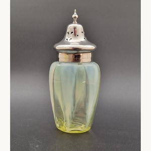 Könnte beinhalten: Ein antiker Glas-Shaker mit silberfarbenem Deckel und dekorativem Knauf. Der Glaskörper hat ein geripptes Design mit gelb-blauer schillernder Oberfläche. Der Deckel hat sternförmige Aussparungen.