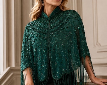 May include: An emerald green capelet featuring intricate beadwork, teardrop-shaped crystals, and a scalloped hemline finished with long, dangling fringe. The garment has a high collar and a sheer, lace-like base fabric adorned with dense embroidery.