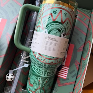 Op de afbeelding: Een groen en rood patroon ge&iuml;soleerde beker met handvat en een FlowState 3-standen deksel. De beker heeft een geometrisch ontwerp, een doorzichtig rietje met een kleine voetbalbedel en een productlabel met dekselfuncties.