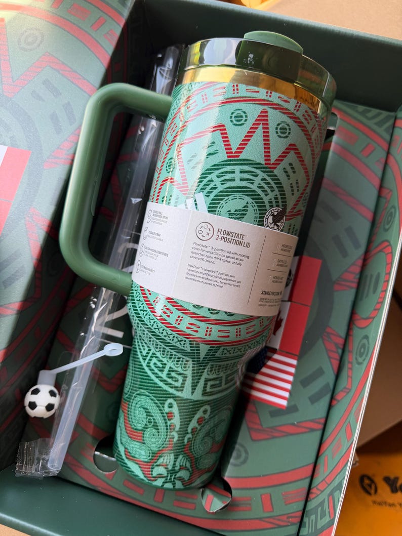 Op de afbeelding: Een groen en rood patroon ge&iuml;soleerde beker met handvat en een FlowState 3-standen deksel. De beker heeft een geometrisch ontwerp, een doorzichtig rietje met een kleine voetbalbedel en een productlabel met dekselfuncties.