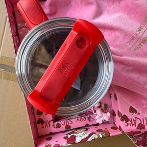 May include: A clear glass container with a red handle and a red lid is inside a pink box with a strawberry design. A pink cloth and small pink accessories are also in the box. The box is inside a larger cardboard box.