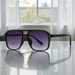 May include: Black square-framed sunglasses with gradient purple lenses. The sunglasses have a double bridge and small silver accents on the temples. The lenses transition from a dark purple at the top to a lighter shade at the bottom.
