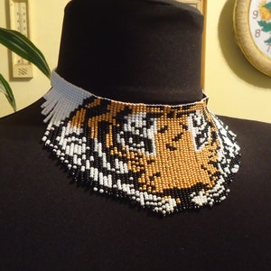 May include: A beaded choker necklace with a tiger face design. The beads are black, white, and gold.