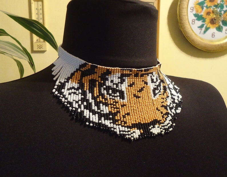 May include: A beaded choker necklace with a tiger face design. The beads are black, white, and gold.