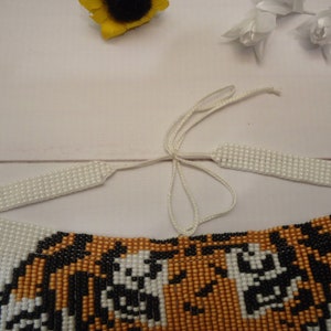 May include: A beaded tiger necklace with white fringe and a white string tie closure.