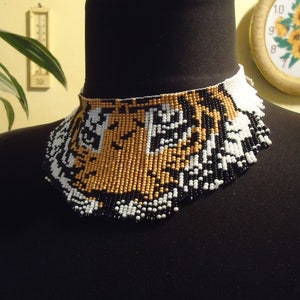 May include: A beaded necklace with a tiger face design. The beads are black, white, and gold.