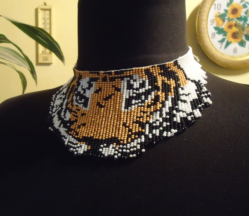 May include: A beaded necklace with a tiger face design. The beads are black, white, and gold.